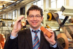 Joachim-Franz Schmidt, Fertigungsleiter Walzwerk bei Heraeus in Hanau, mit dem Bauteil eines walzplattierten Bandes von Heraeus (rechts) und dem Beschleunigungsrohr für den Large Hadron Collider. Der speziell hergestellte Sonderstahl für die Bänder wurde von Heraeus mit einer hauchdünnen Kupferschicht von nur wenigen Mikrometern Dicke plattiert und gleichzeitig mit einem Sägezahn-Spezialprofil versehen. Die Sägezähne dienen der Reflexion der bei den späteren Experimenten aus der Teilchenkollision freigesetzten Strahlung. (Foto: Heraeus) Joachim-Franz Schmidt, Fertigungsleiter Walzwerk bei Heraeus in Hanau, mit dem Bauteil eines walzplattierten Bandes von Heraeus (rechts) und dem Beschleunigungsrohr für den Large Hadron Collider. Der speziell hergestellte Sonderstahl für die Bänder wurde von Heraeus mit einer hauchdünnen Kupferschicht von nur wenigen Mikrometern Dicke plattiert und gleichzeitig mit einem Sägezahn-Spezialprofil versehen. Die Sägezähne dienen der Reflexion der bei den späteren Experimenten aus der Teilchenkollision freigesetzten Strahlung. (Foto: Heraeus)