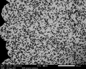REM-Aufnahme des Metall-Keramik Gefüges. Die groben Keramik-Partikel (schwarz) sind nahezu homogen in der dichten metallischen Matrix eingebettet. 