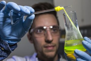 © Silvia SteinbachEin Mitarbeiter zieht im Labor für Systembiotechnologie an der Universität des Saarlandes einen Bionylonfaden aus einem Glaskolben.